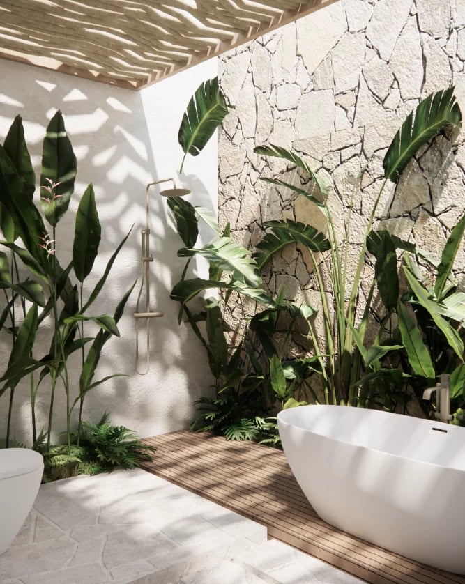 Modern outdoor bathroom with freestanding white bathtub, lush green plants, cracked white stone wall, and wooden deck flooring