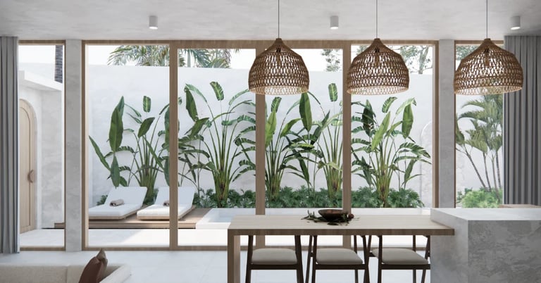 Modern dining room with wood table and chairs, large glass doors opening to patio with tropical plants, woven pendant lights overhead